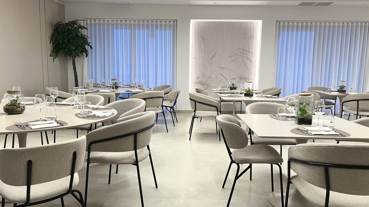 Ristorante e Pizzeria: tavoli apparecchiati con poltroncine chiare davanti a grandi finestre