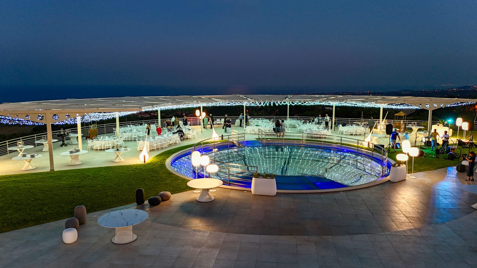 Sala Miramar all’imbrunire: la piscina circolare illuminata e i tavoli all’aperto davanti al mare