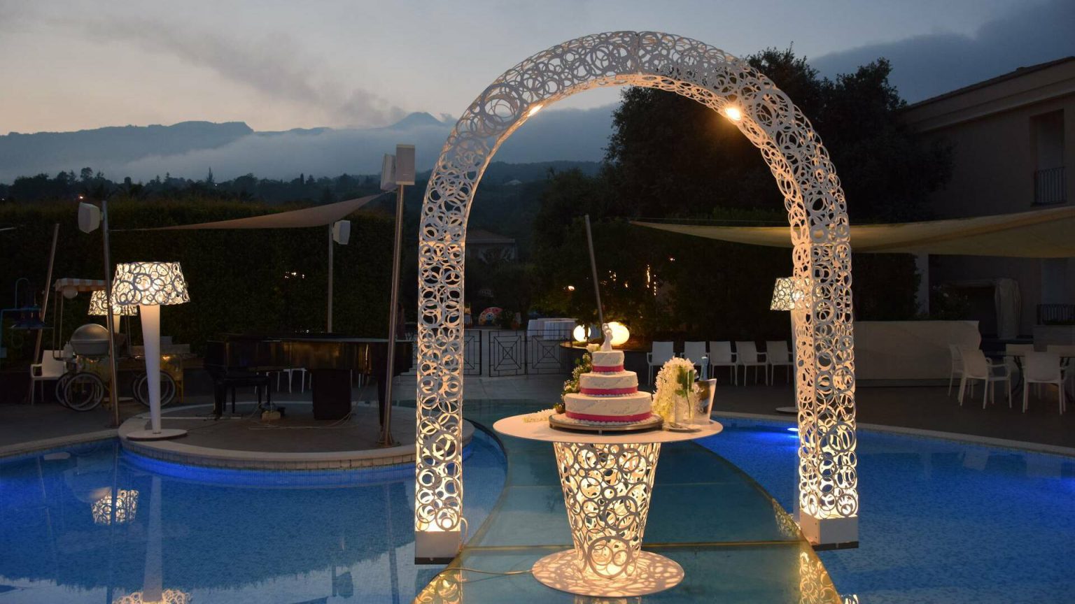 Sala Aurora Garden: arco luminoso e tavolo della torta a bordo piscina, di sera