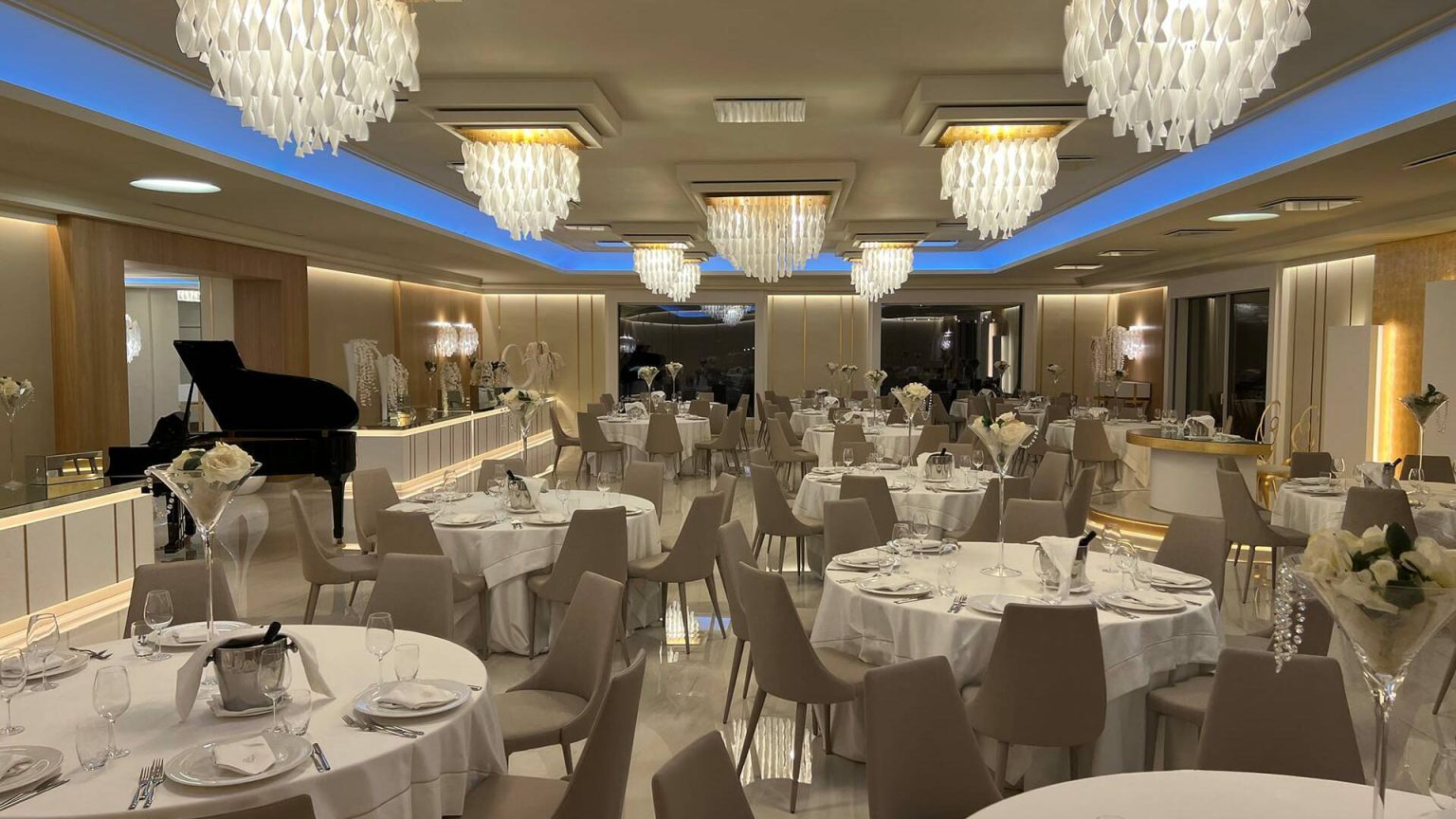 Sala Luxury: lampadari di cristallo, tavoli rotondi apparecchiati e un pianoforte a coda